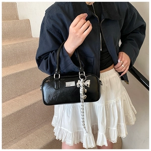 Detail of a black patent leather Boston bag with silver bow charm and metal plaque