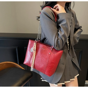 Detail of red pebbled leather tote featuring gold lettering and a woven charm ornament