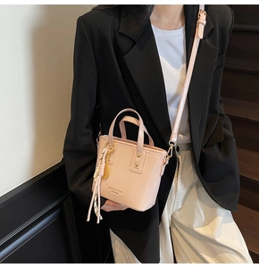 Detail of light pink mini bucket bag featuring textured leather and woven charm