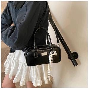 Detail of a shiny black Boston bag with silver butterfly pendant and woven tassel charm