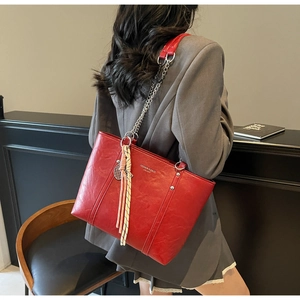 Detail of red leather tote bag with gold chain strap and decorative tassel charm