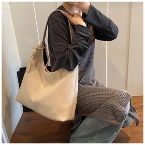Chic cream beige leather tote bag shown on shoulder in a minimalist indoor setting