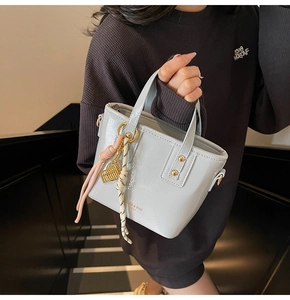 Close-up of light grey patent leather bucket bag with gold charms and ribbon detail