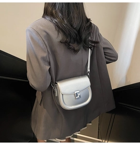 Close-up of metallic silver saddle bag worn cross-body with a sleek metal twist lock