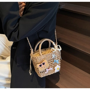 Detail of woven straw bucket bag with cute bear charm and drawstring lining on wooden stairs