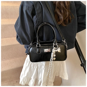 Close-up of black patent leather Boston bag with silver hardware and bow charm detail