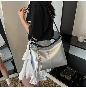 Detail view of silver tote bag with metallic sheen, triangle plaque and woven keychain