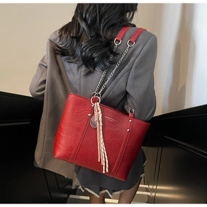 Detail of red leather tote bag with silver chain strap and fashionable tassel ornament