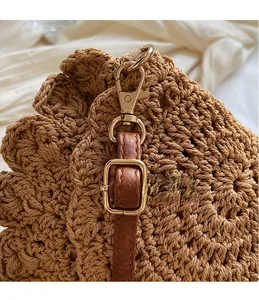Détail du crochet en métal doré et de la bandoulière en cuir brun sur le sac tressé