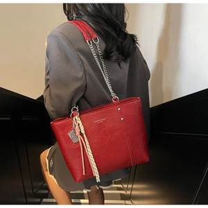 Detail of red leather tote bag featuring silver chain strap and decorative charms