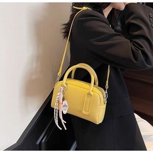Detail of yellow lychee leather Boston bag with decorative charm and shoulder strap