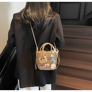 Detail of woven straw bucket bag featuring cute bear charms and colorful bows decoration