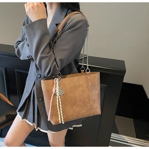 Detailed side view of a brown leather tote bag with chain strap and woven charm