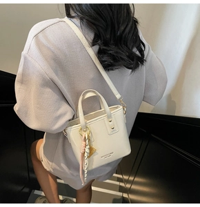 Detail of cream bucket bag with silk scarf accessory and brand logo shown on model