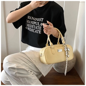 Detail of creamy yellow Boston bag featuring lychee grain leather and heart ribbon charm