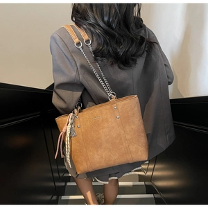 Brown leather tote bag detail with silver chain strap and metal rivet accents