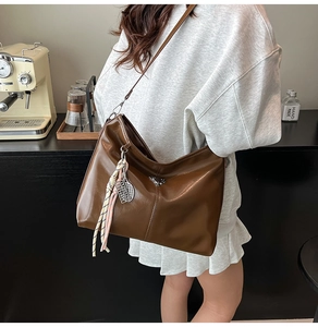 Close-up of brown leather hobo bag with V-shaped metal buckle and woven tassel detail