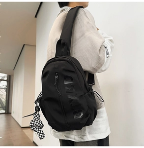 Detail of black nylon chest bag with vertical zipper and checkerboard charm accessory