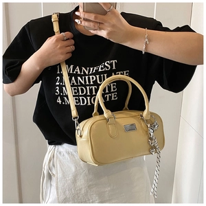 Close-up of cream Boston bag with heart charm and woven strap details in mirror view