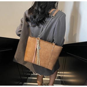 Detailed view of brown tote bag with metal chain strap and decorative stitching