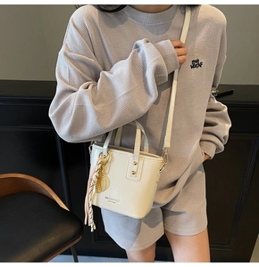 Close-up of cream leather bucket bag with metallic leaf charm and brand logo detail