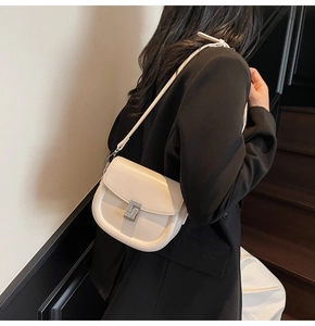 Detail of a creamy beige leather saddle bag with silver square buckle worn with black suit