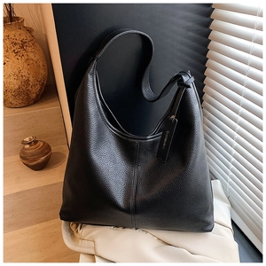 Detail of black pebbled leather hobo bag with wide strap and branded charm tag