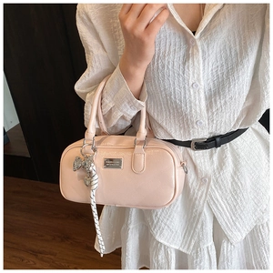 Close-up of peach pink patent leather Boston bag with silver bow and woven pendant details