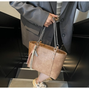 Brown leather tote bag featuring a silver metal chain and colorful braided pendant