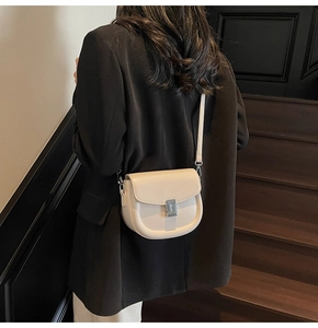 Model view showing a cream leather saddle crossbody bag with silver metal lock closure