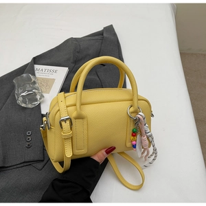 Detail of a bright yellow litchi pattern cylinder handbag with stylish colorful charms