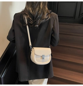 Detail of cream saddle crossbody bag with silver buckle worn over black blazer