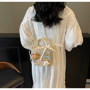 Close-up of woven bucket bag with floral daisy decor and plush bear charm on white dress