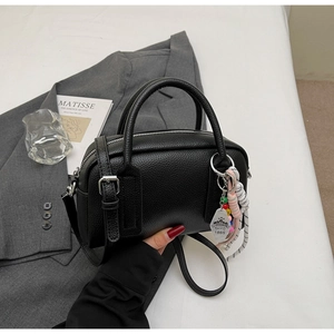 Detail of black lychee grain leather mini Boston bag with decorative bead keychain on a blazer