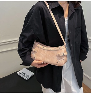 Détail d'un sac bandoulière beige clair avec clous argentés porté par un mannequin
