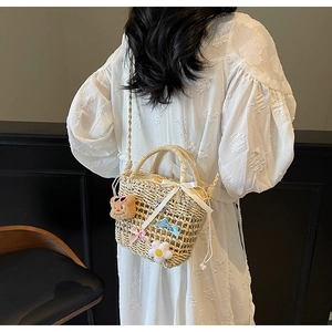 Detail of woven straw bucket bag with white satin bow, bear charm and drawstring closure