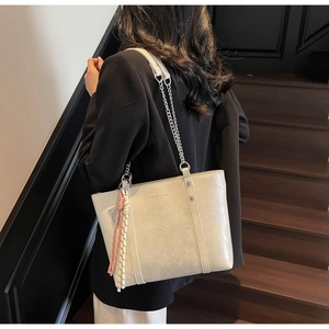 Detail of light beige leather tote bag with chain strap and woven charm on model