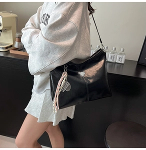 Close-up of black glossy leather tote bag with silver triangle logo and tassel detail