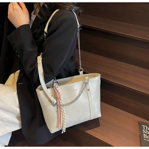 Close-up of cream tote bag with metal chain detail and woven tassel on wooden stairs