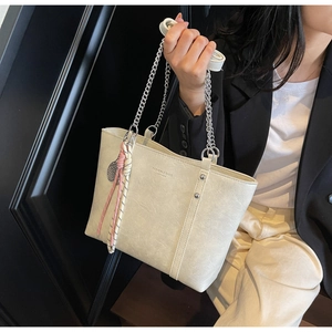 Detail of cream leather tote bag with silver chain strap and braided charm accent