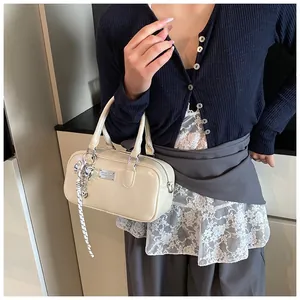 Close-up of beige Boston bag featuring a silver metal plate and heart pendant accessory