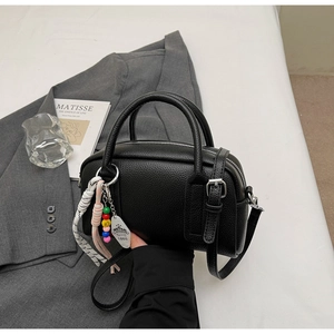 Detail of black lychee grain boston bag with decorative charms and silver hardware