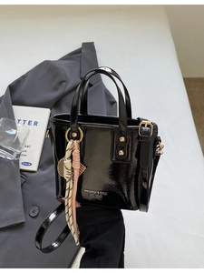 Elegant black patent leather bucket bag with gold hardware and a silk scarf charm
