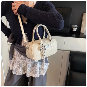 Detail of cream Boston bag with glossy finish and silver bow charm shown on model