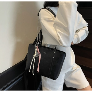 Detail of black leather tote bag with silver chain strap and decorative charm pendant