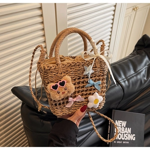 Detail of woven straw bucket bag with plush bear, satin bows, and white floral charms