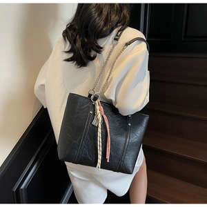 Detail of black oil-wax leather tote with silver chain strap and woven charm on a model