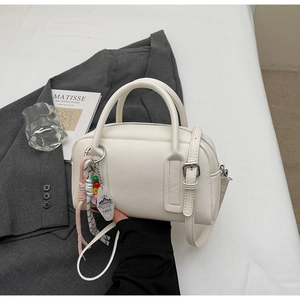 Close-up of off-white lychee pattern leather bag with decorative beaded charm and straps