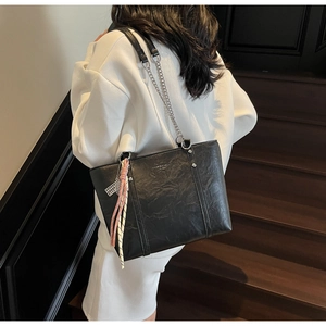 Detail of black tote bag featuring textured leather, silver chain and pink tassel charm