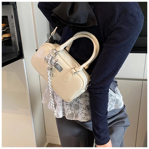 Close-up of cream Boston bag with fine ribbon, heart pendant and silver logo plate